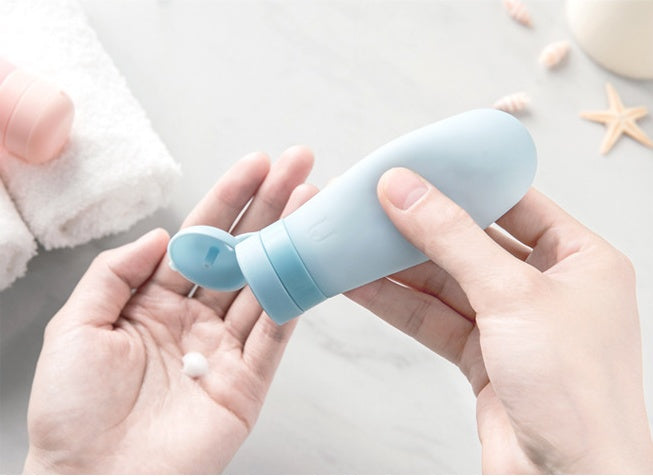 Shopi Vella blue silicone travel bottles being squeezed to dispense lotion onto hand over marble surface