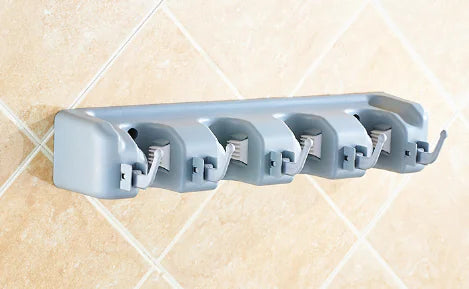 Gray wall-mounted mop and broom holder with five adjustable grips installed on a tiled wall