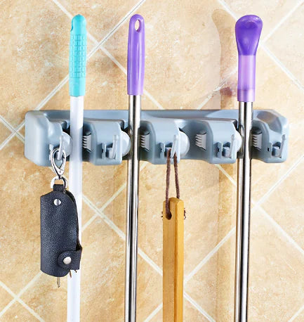 Wall-mounted mop and broom holder organizing three cleaning tools with gray grips on tiled wall