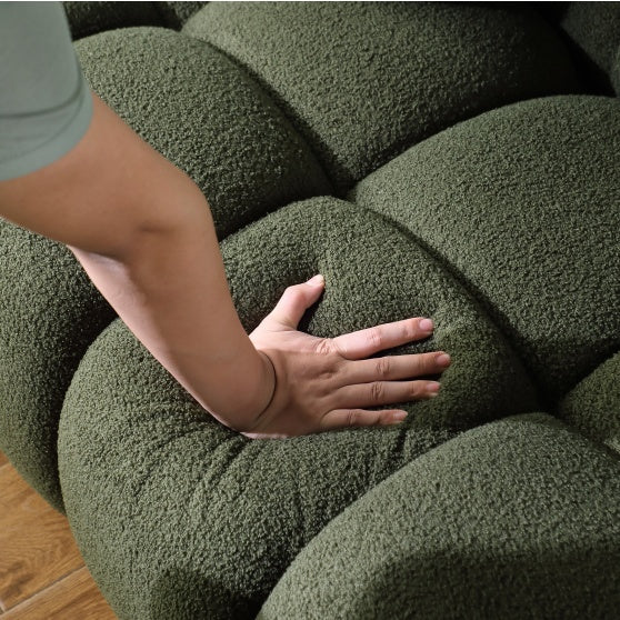 Close-up of a hand pressing on the soft surface of a green upholstered sofa by Shopi Vella