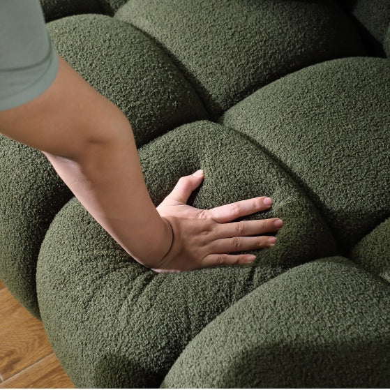Close-up of hand pressing soft cushion on green upholstered sofa by Shopi Vella