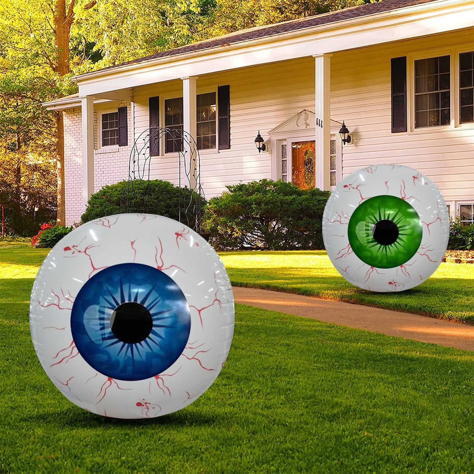 Two large Halloween eyeball balloon decorations with blue and green irises on a front lawn