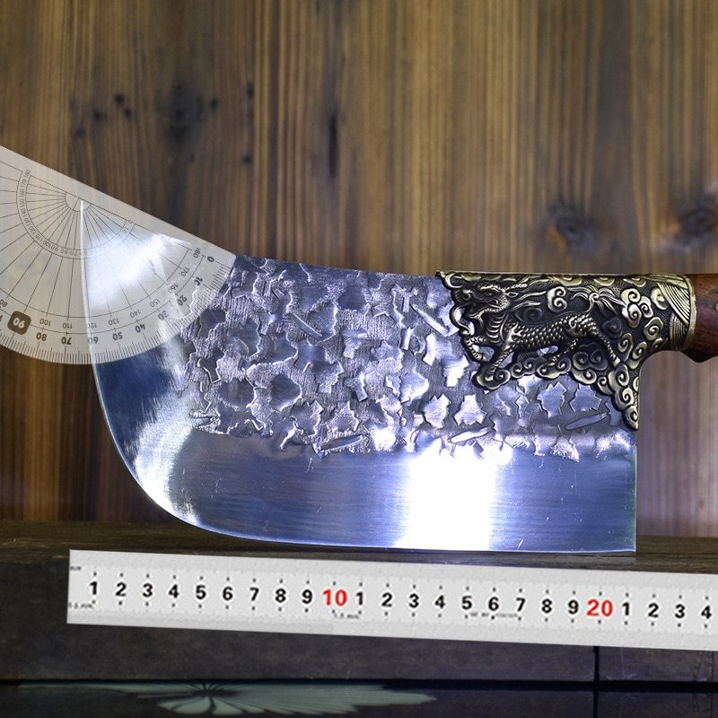 Hand-forged bone chopping knife with textured blade and ornate handle placed above a ruler