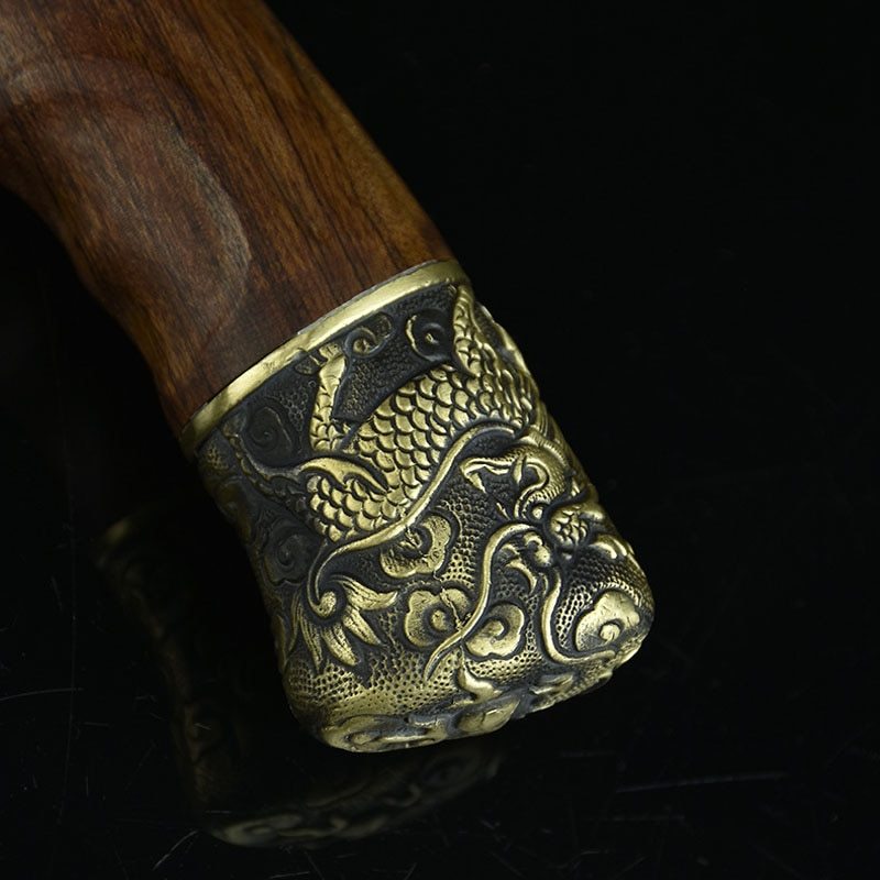 Close-up of hand-forged bone chopping knife wooden handle with detailed engraved brass dragon design