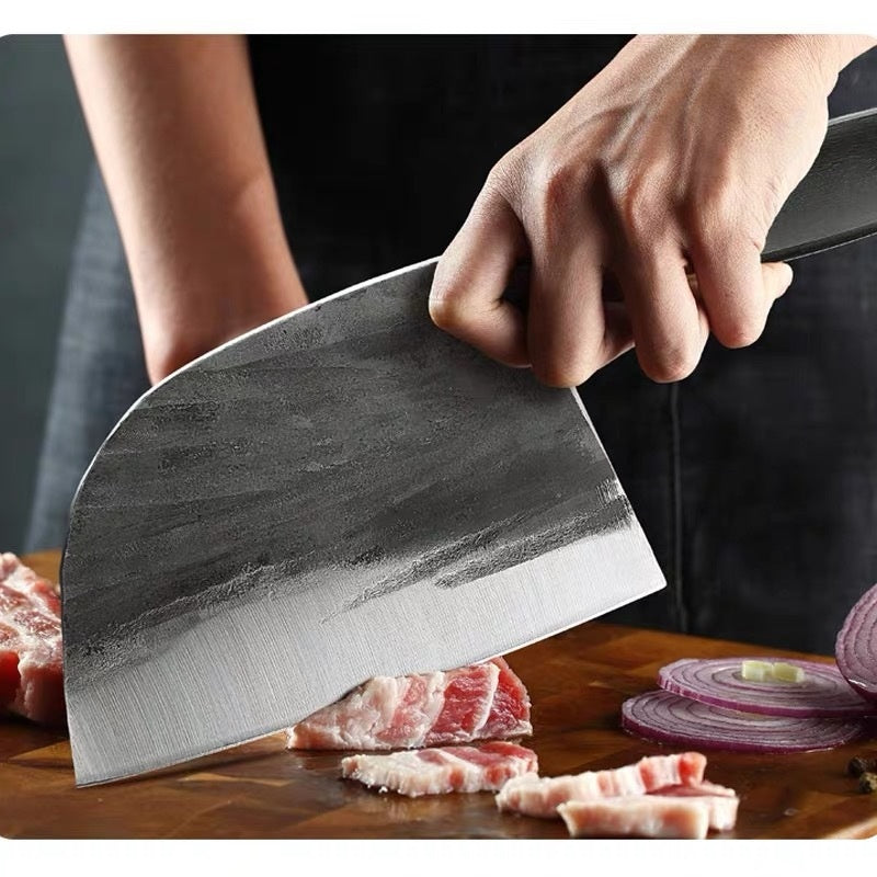 Hand holding a hand-forged kitchen slicing knife cutting meat and onions on wooden board