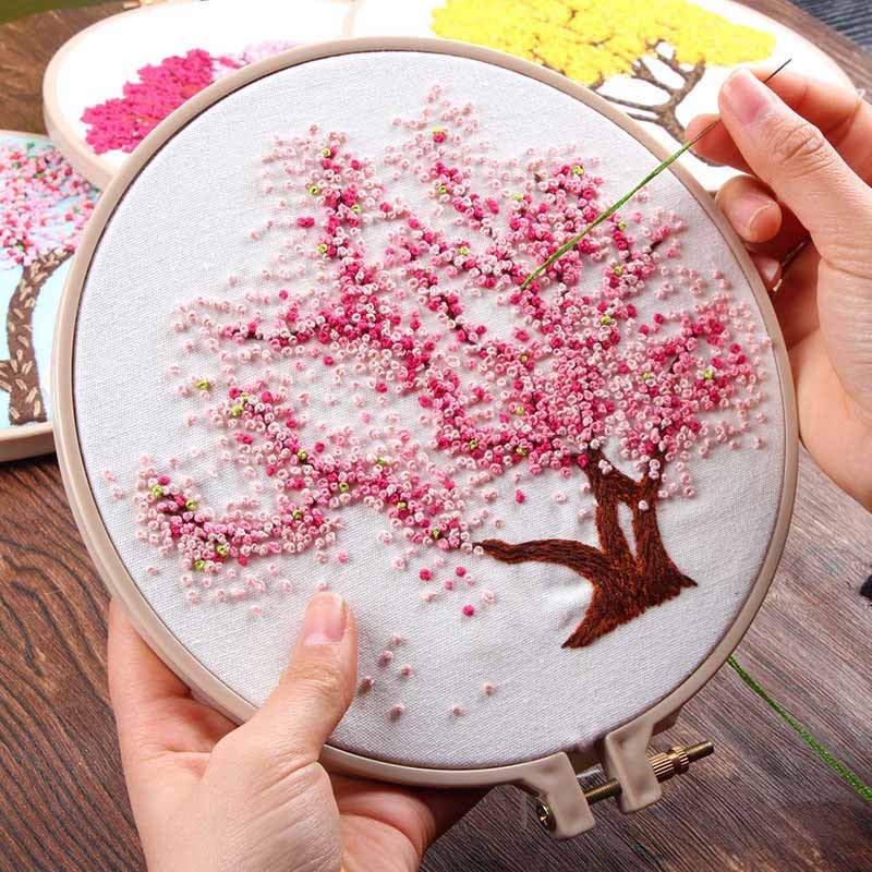 Hand stitching pink blossom tree on fabric hoop showing handmade embroidery wall art technique