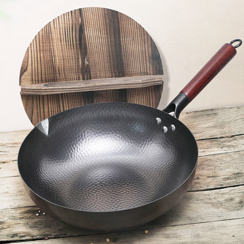 Shopi Vella handmade iron wok with hammered texture and wooden handle on rustic wooden surface