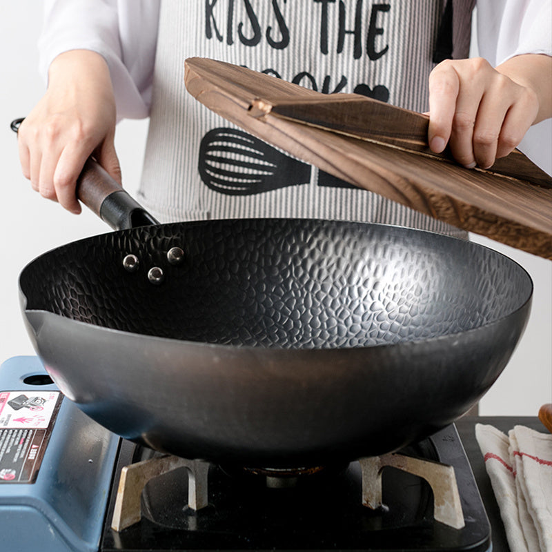 Shopi Vella handmade iron wok with textured surface on stovetop being opened with wooden lid