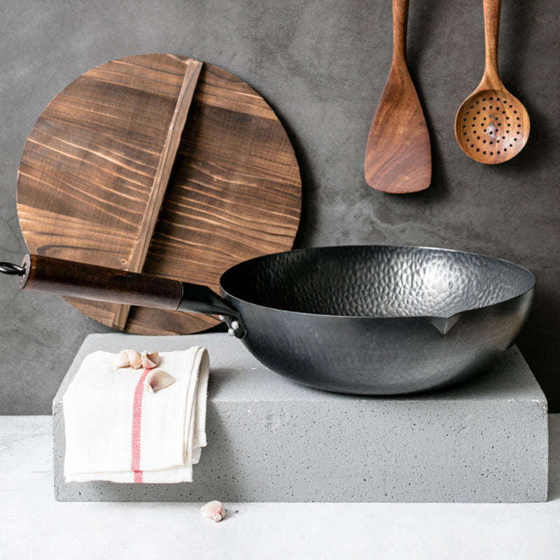 Shopi Vella handmade iron wok with wooden handle displayed with wooden utensils and cutting board
