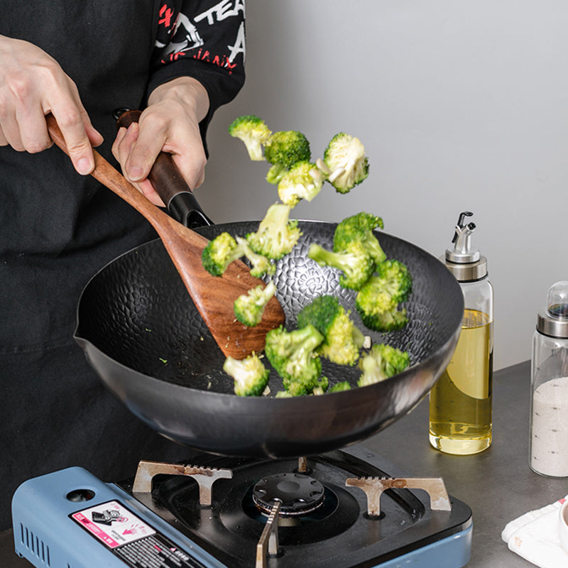 Cooking broccoli stir fry in handmade iron wok on gas stove with wooden spatula by Shopi Vella