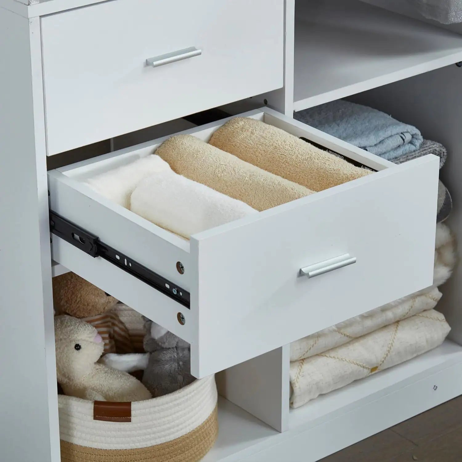 White drawer organizer with folded towels and plush toys in a hanging rod closet organizer for bedroom