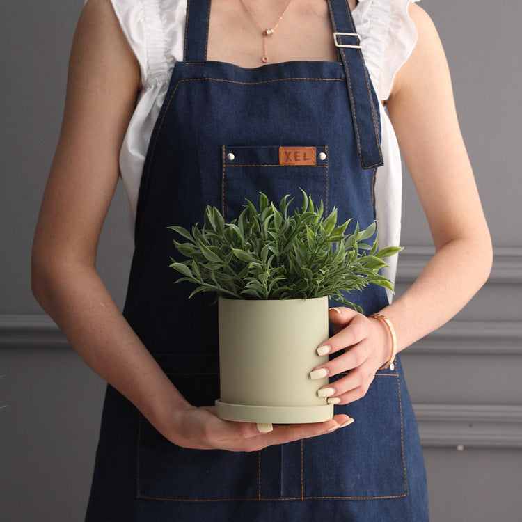 Person holding green industrial style planter pot with lush green plant indoors
