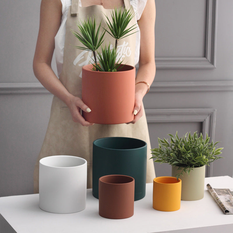 Shopi Vella industrial style planter pot in terracotta held by person with various colorful planter pots on table