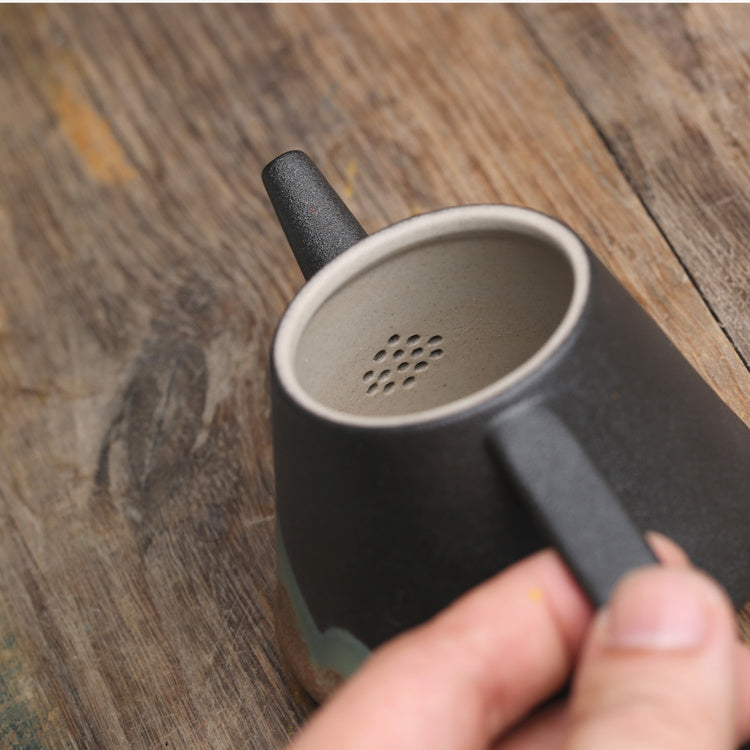 Close-up of a black Japanese ceramic teapot spout and handle held over wooden surface