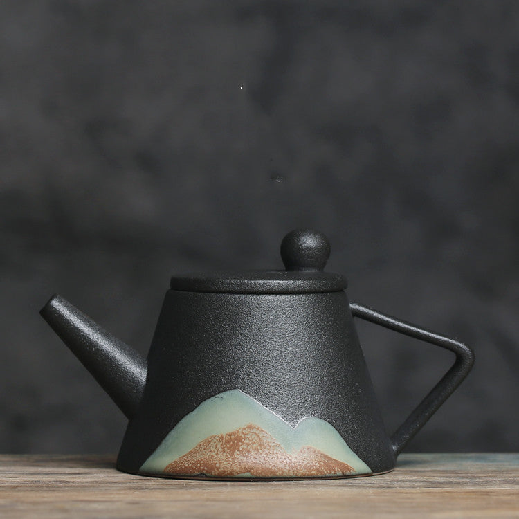 Black Japanese ceramic teapot with mountain design and angled handle on wooden surface