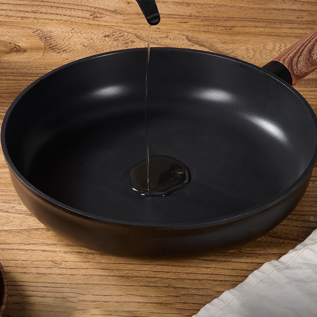 Non stick pots and pans with removable handles showing oil being poured into a black frying pan on a wooden surface