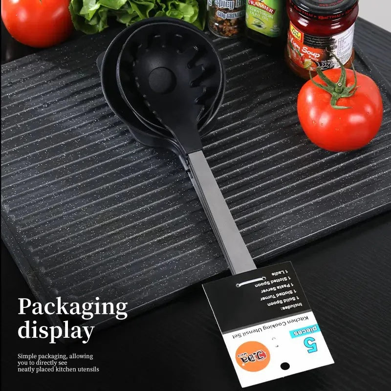 Shopi Vella kitchen utensil gift set with black spoon and ladle on a textured black surface with fresh tomatoes and herbs