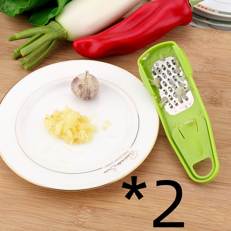 Shopi Vella green garlic masher kitchen tool with crushed garlic on white plate and fresh vegetables