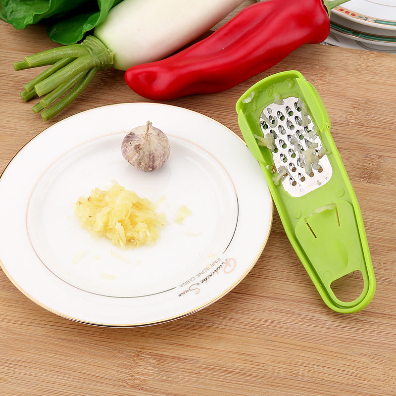 Shopi Vella green garlic masher kitchen tool with crushed garlic on plate and fresh vegetables