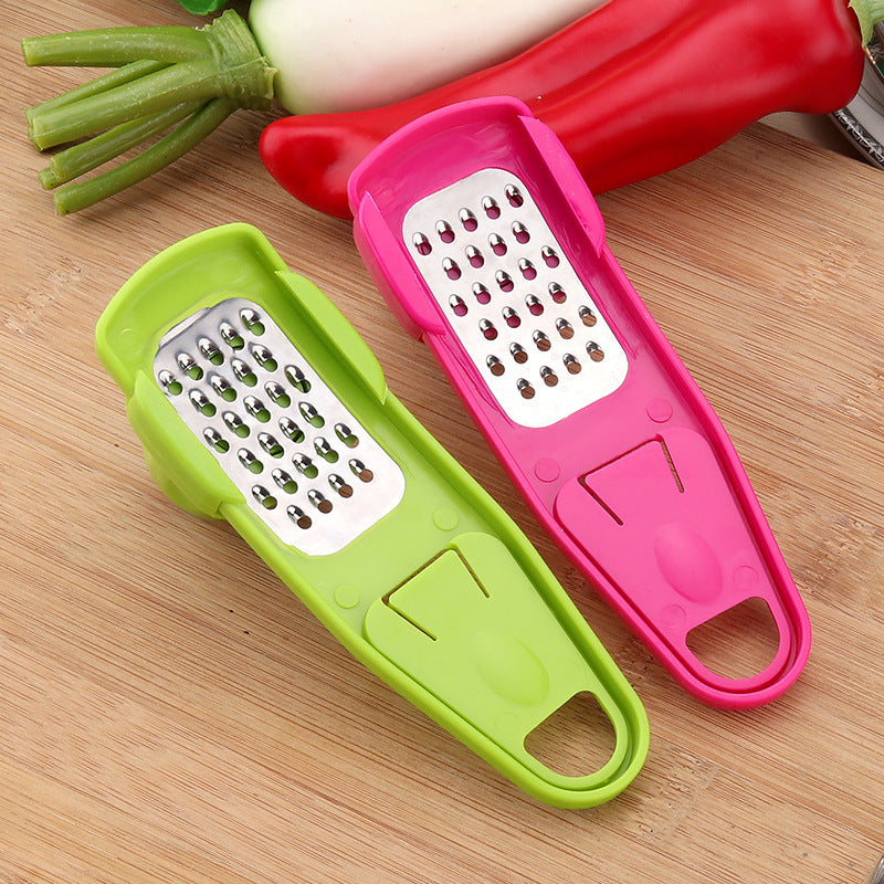 Green and pink garlic masher kitchen tool with stainless steel grating surfaces on wooden cutting board