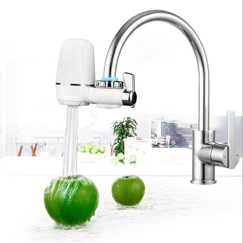 Modern silver kitchen faucet water filter attached to a kitchen sink with water flowing over a green apple