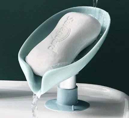 Leaf shaped soap holder in light blue with drainage pouring water and white bar soap on top