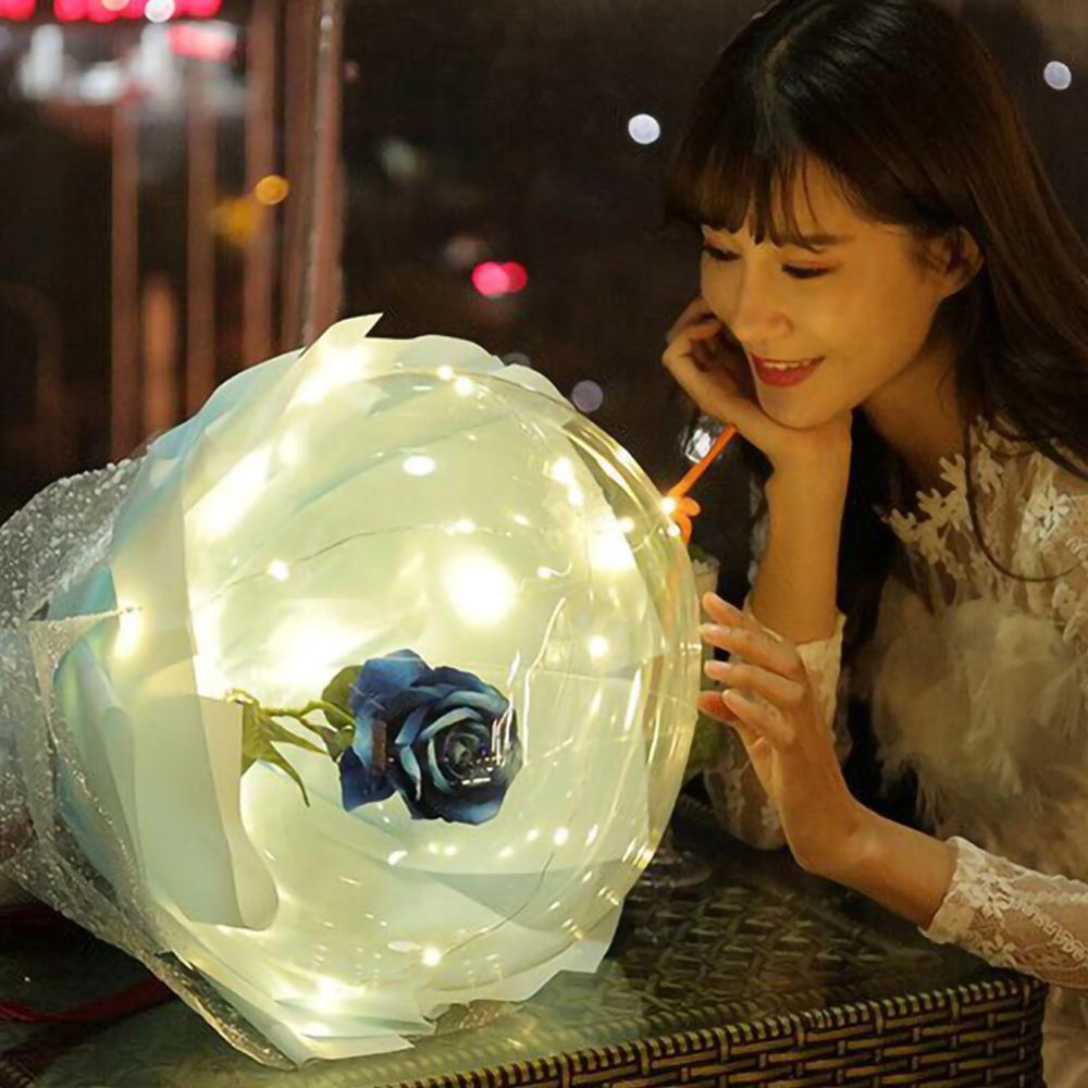 Woman admiring a glowing LED rose balloon bouquet with white lights in transparent wrapping