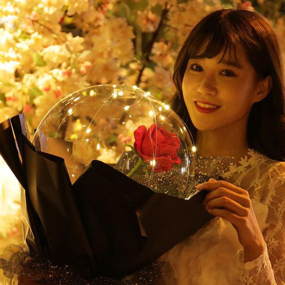 Woman holding LED rose balloon bouquet with glowing lights and red rose wrapped in black paper