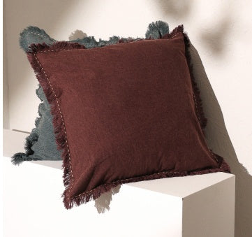 Shopi Vella linen pillow with fringe edges in brown and blue colors displayed on white geometric surfaces
