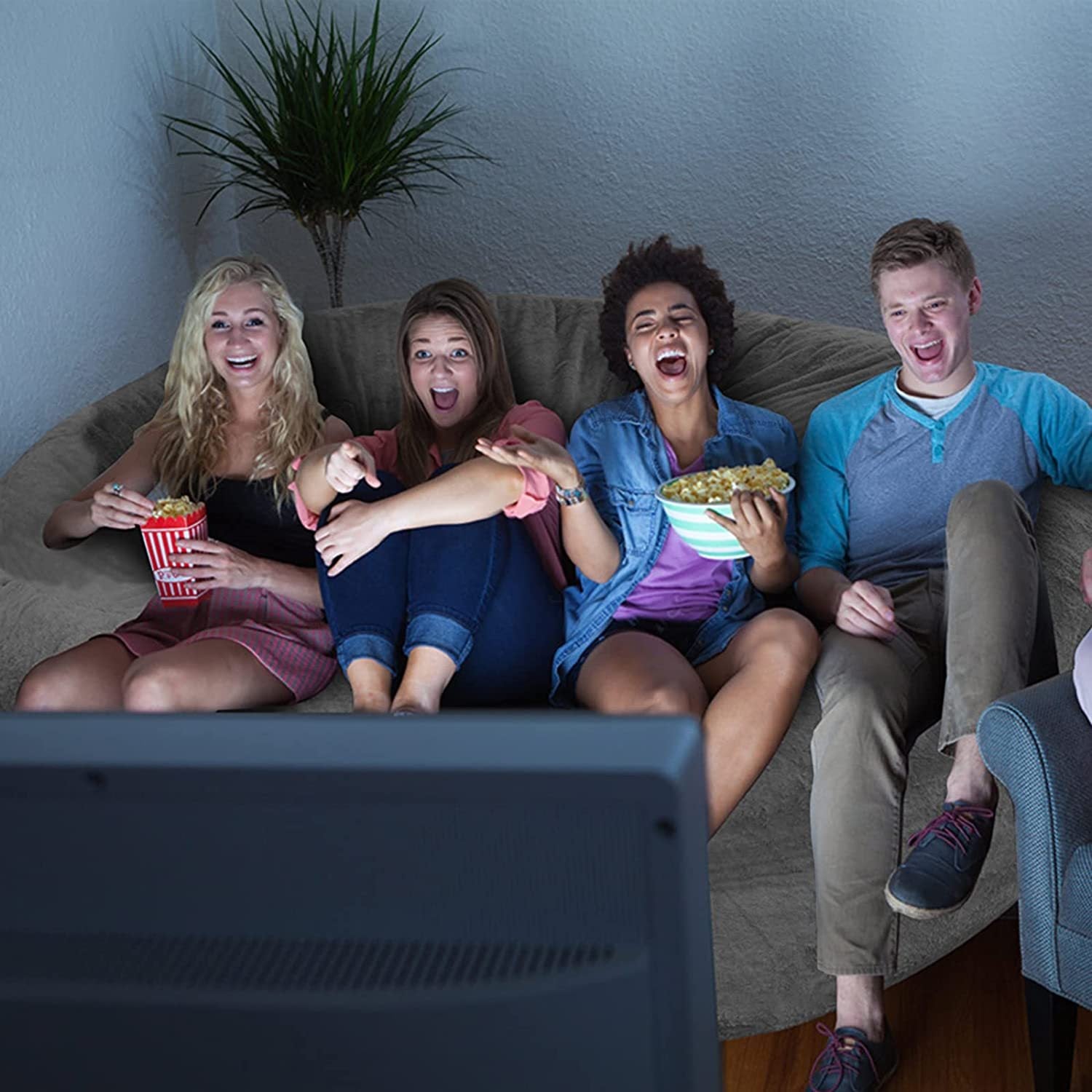 Four friends sitting comfortably on a living room bean bag cushion cover watching TV and enjoying snacks
