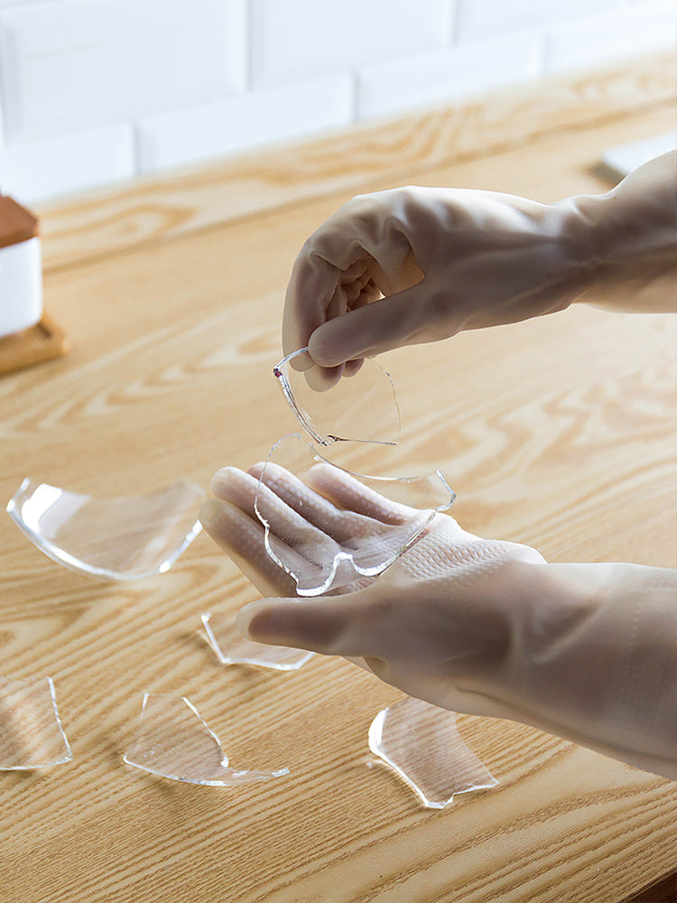 Hands wearing long nitrile dishwashing gloves handling broken glass pieces on wooden surface