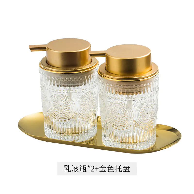 Luxury glass soap dispenser set with two embossed clear glass bottles and gold pump lids on gold tray