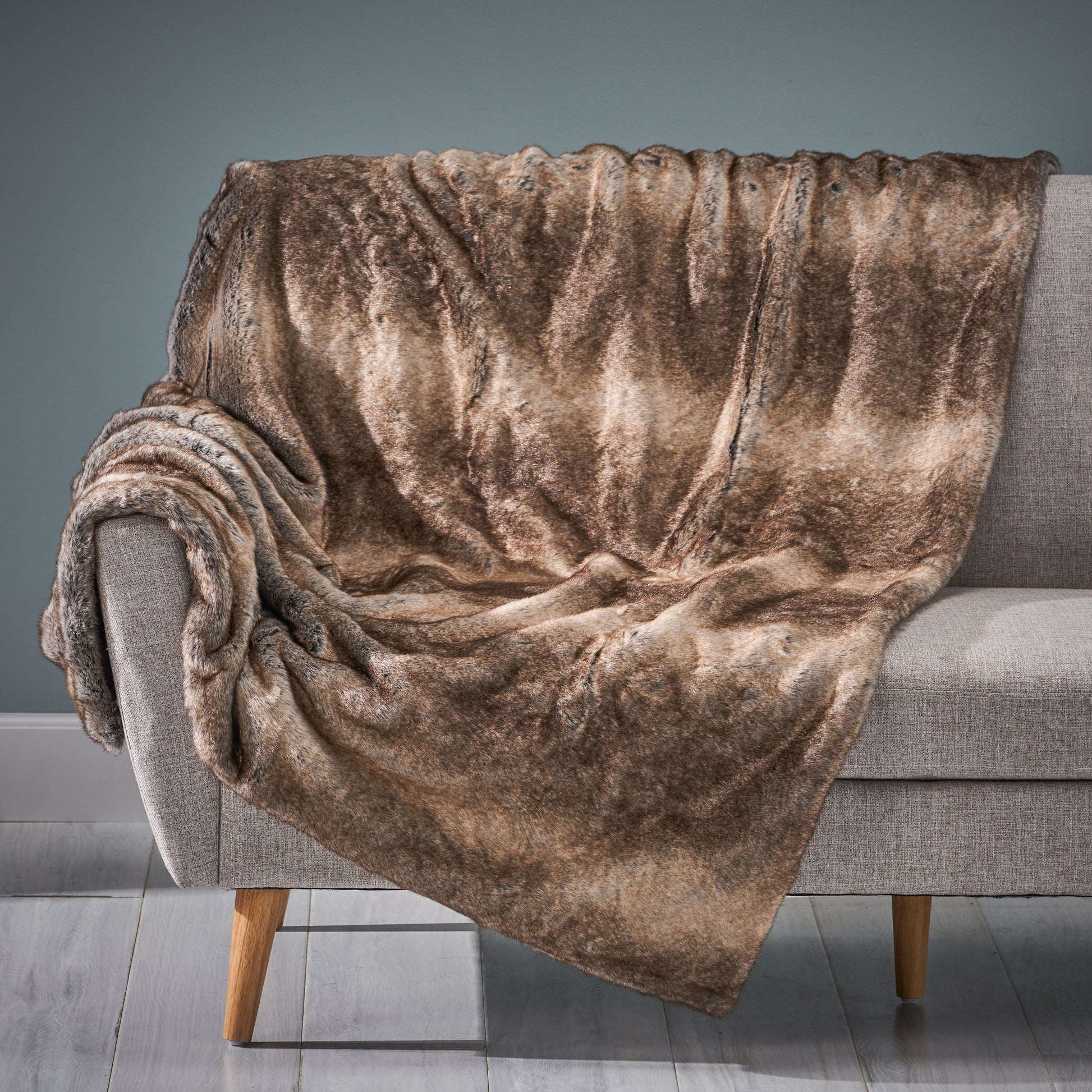 Brown plush luxury living room blanket draped over gray modern sofa with wooden legs
