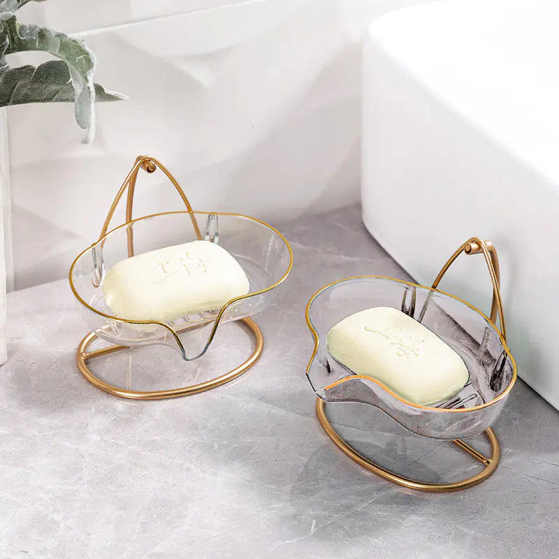 Luxury soap holder with drainage in clear design and gold frame holding white soap bars on gray countertop