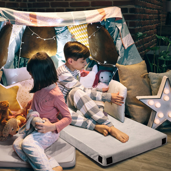 Two kids sitting on a memory foam mattress topper in a cozy indoor tent setup with pillows and stuffed animals