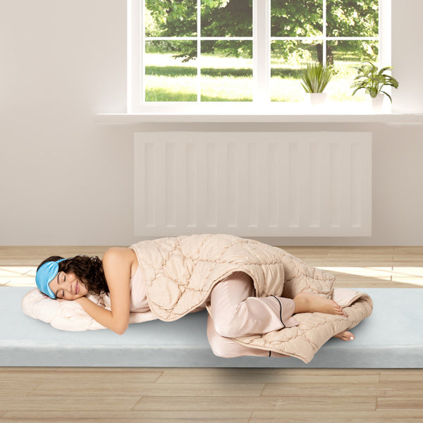 Woman sleeping comfortably on memory foam mattress topper with beige quilt and blue sleep mask