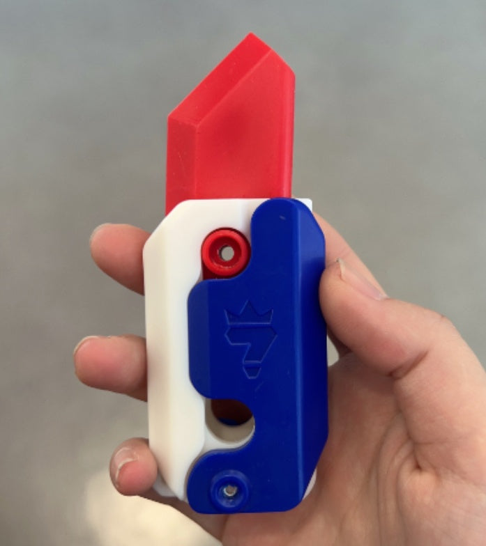 Hand holding a Shopi Vella mini 3D printing toy knife with red, white, and blue colors