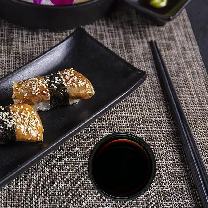 Mini condiment dipping bowls with soy sauce served alongside sushi on black plate with chopsticks