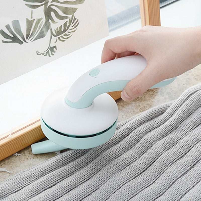 Shopi Vella mini desktop vacuum cleaner in white and mint green cleaning dust from a grey knitted fabric