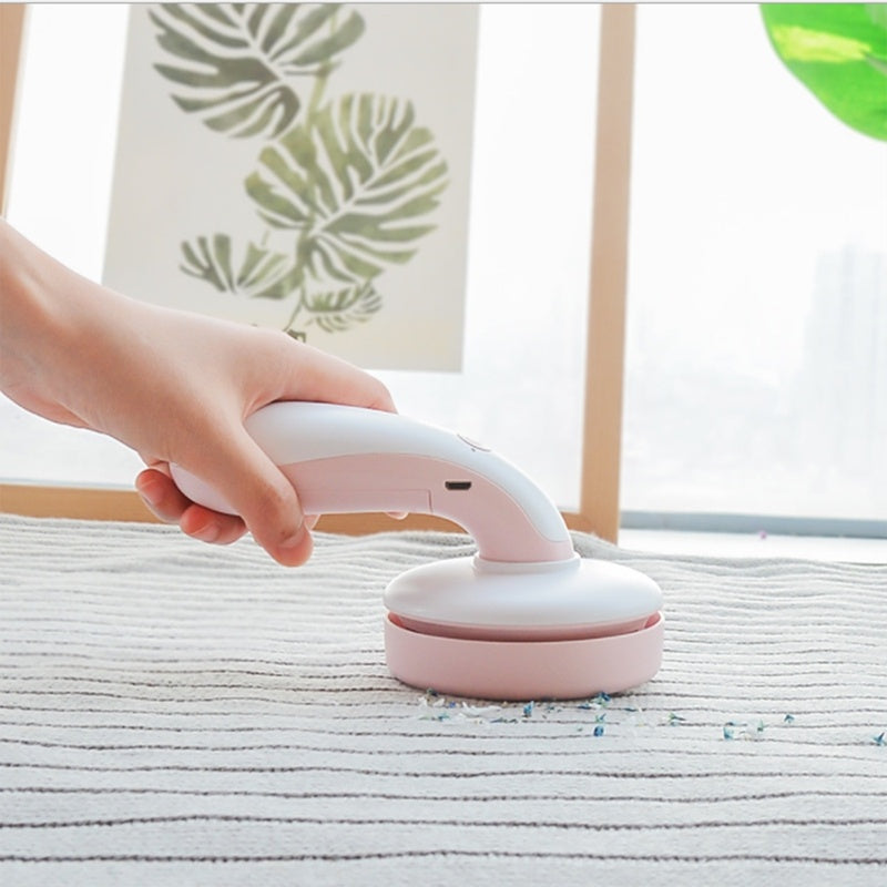 Shopi Vella mini desktop vacuum cleaner in white and pink being used to clean small debris on a fabric surface