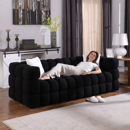 Shopi Vella modern fabric sofa for living room in black with cushioned block design and a woman relaxing on it