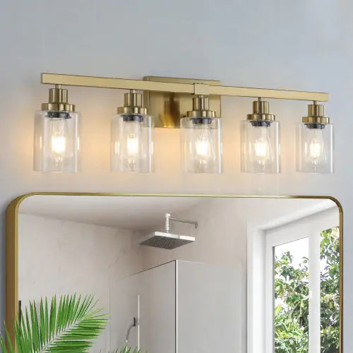 Modern gold vanity light fixture with five clear glass shades mounted above a bathroom mirror