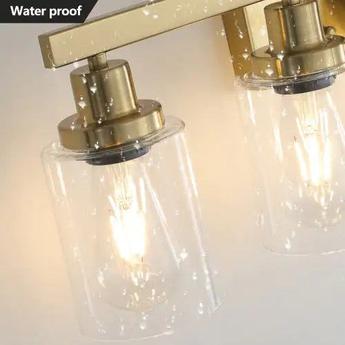 Waterproof modern gold vanity light fixture with clear cylindrical glass shades and warm LED bulbs