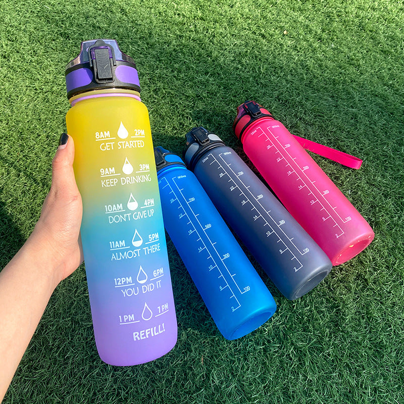 Shopi Vella motivational water bottle with time marker in gradient purple and yellow held in hand with three other colorful bottles on grass