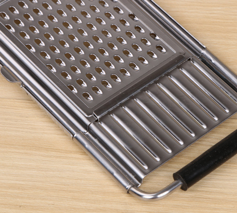 Shopi Vella multi-purpose grater and peeler with stainless steel blades and black handle on wooden surface