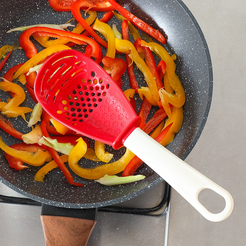 Shopi Vella multifunctional slotted cooking spoon with red head and white handle in frying pan with sliced bell peppers