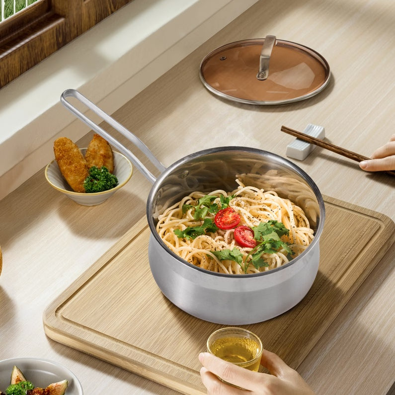 Shopi Vella non-stick stainless steel saucepan with cooked noodles and vegetables on a wooden board