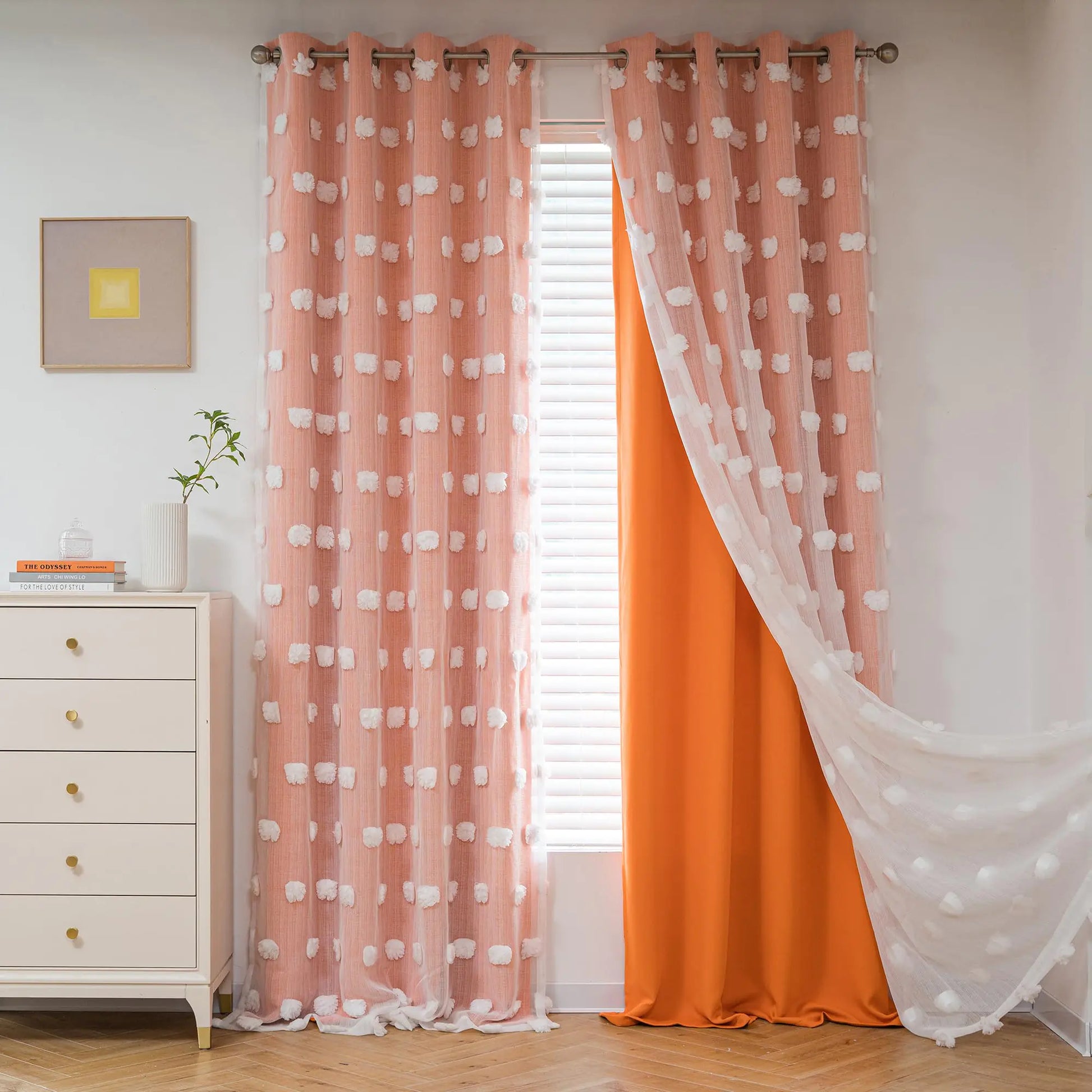 Pink nursery pom pom sheer curtains with white pom poms layered over solid orange curtains in a modern nursery