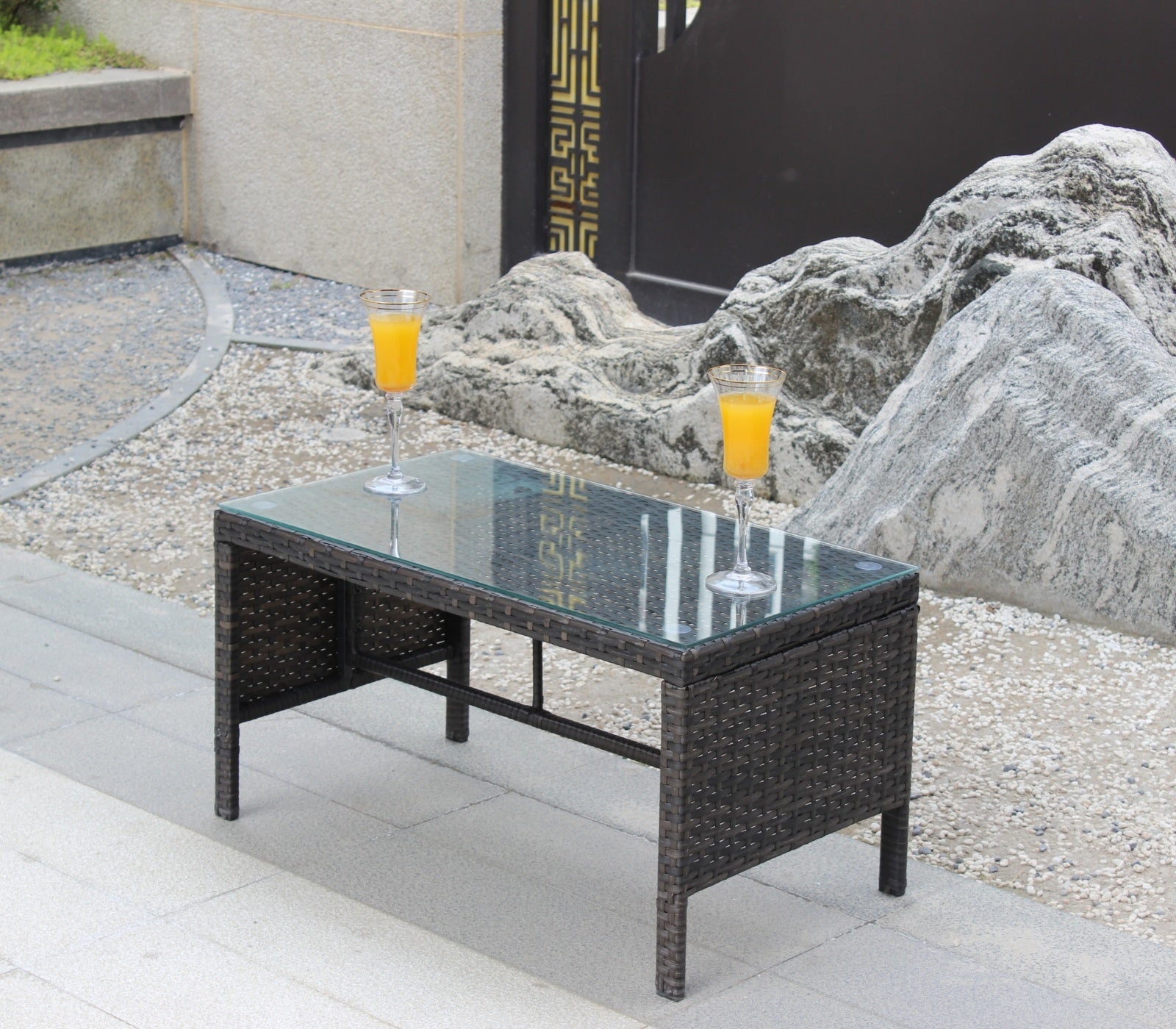 Shopi Vella outdoor patio coffee table with glass top and woven rattan design set on stone patio