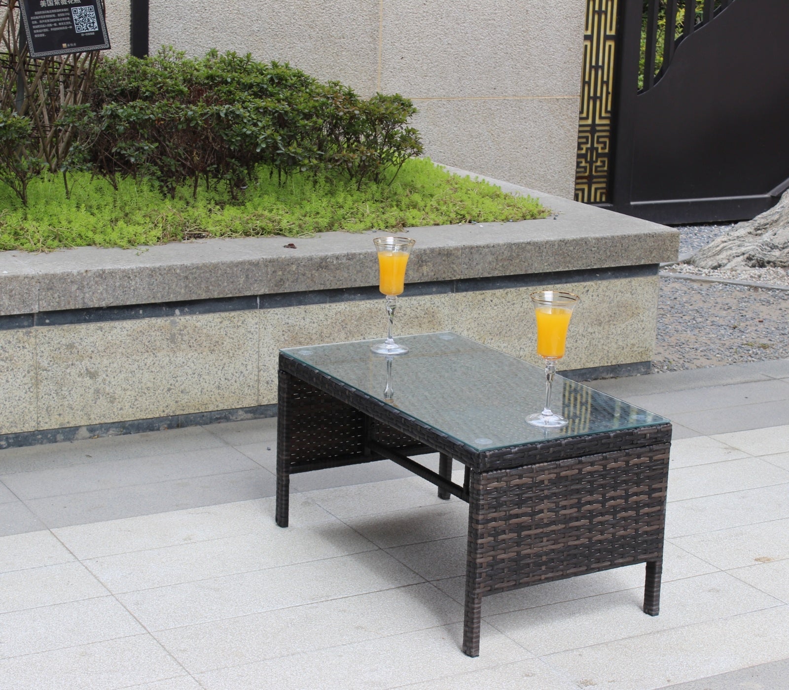 Shopi Vella outdoor patio coffee table with glass top and dark woven rattan design on tiled patio